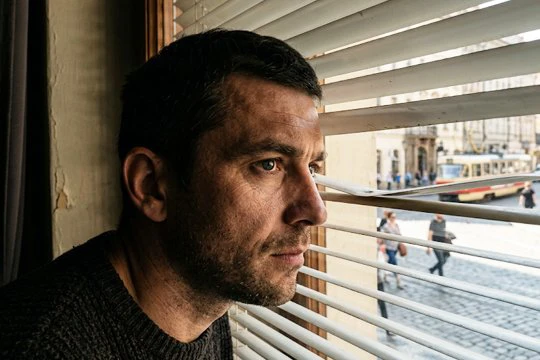 Мужчина тревожно смотрит через жалюзи